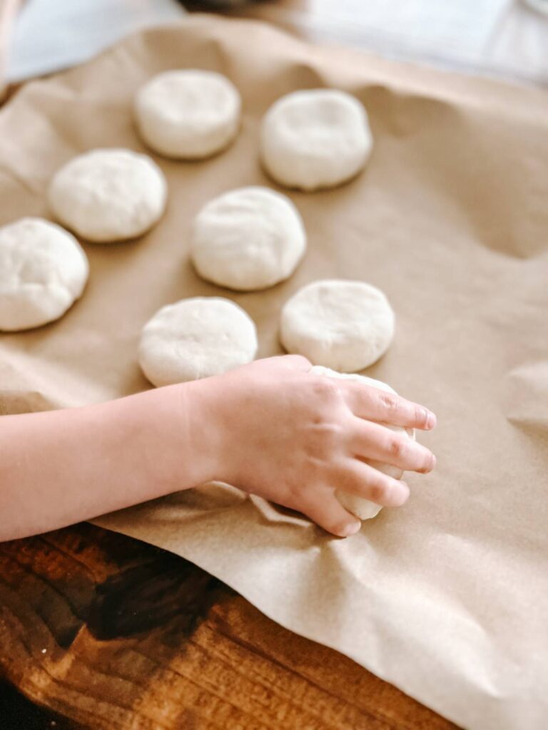 hand placing disks of bread dough onto cookie sheet with parchment paper.