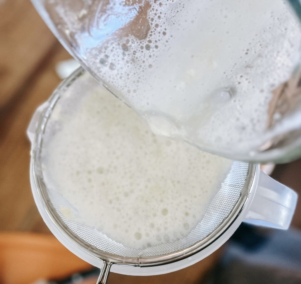Limeade being poured into a pitcher through a strainer.