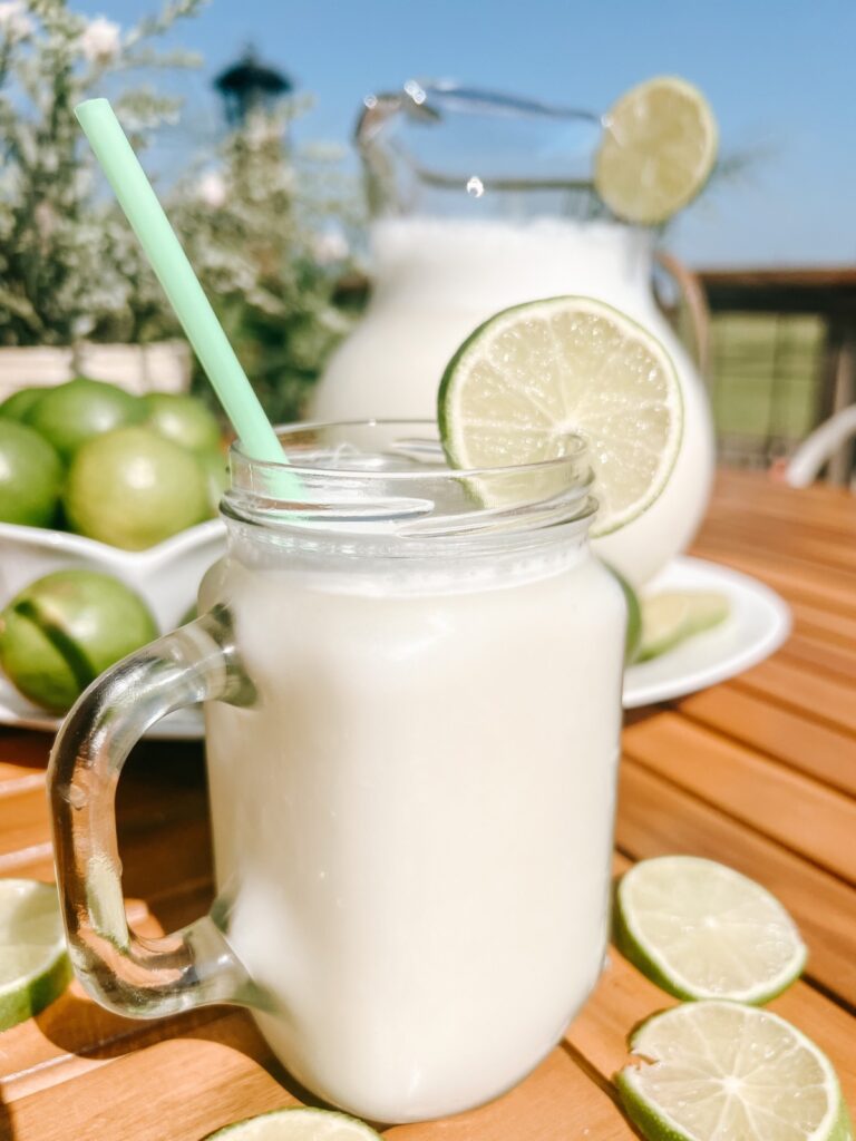 Outside on a table, Brazilian Limeade in a glass cup and pitcher with limes all around.
